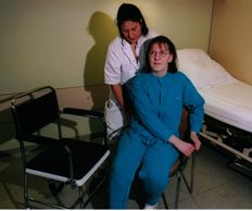 Die Pat. greift die körperferne Stuhllehne, die Pflegekraft führt ihr Becken